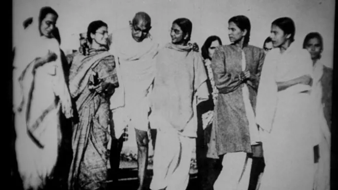 Gandhi is surrounded by his female followers, receiving their support as he walks.